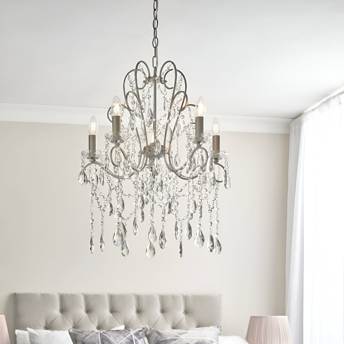 Endon Aldwood 5 light pendant in aged silver with faceted crystal droplets and scrolled metalwork, hung above a bed with a tufted headboard.