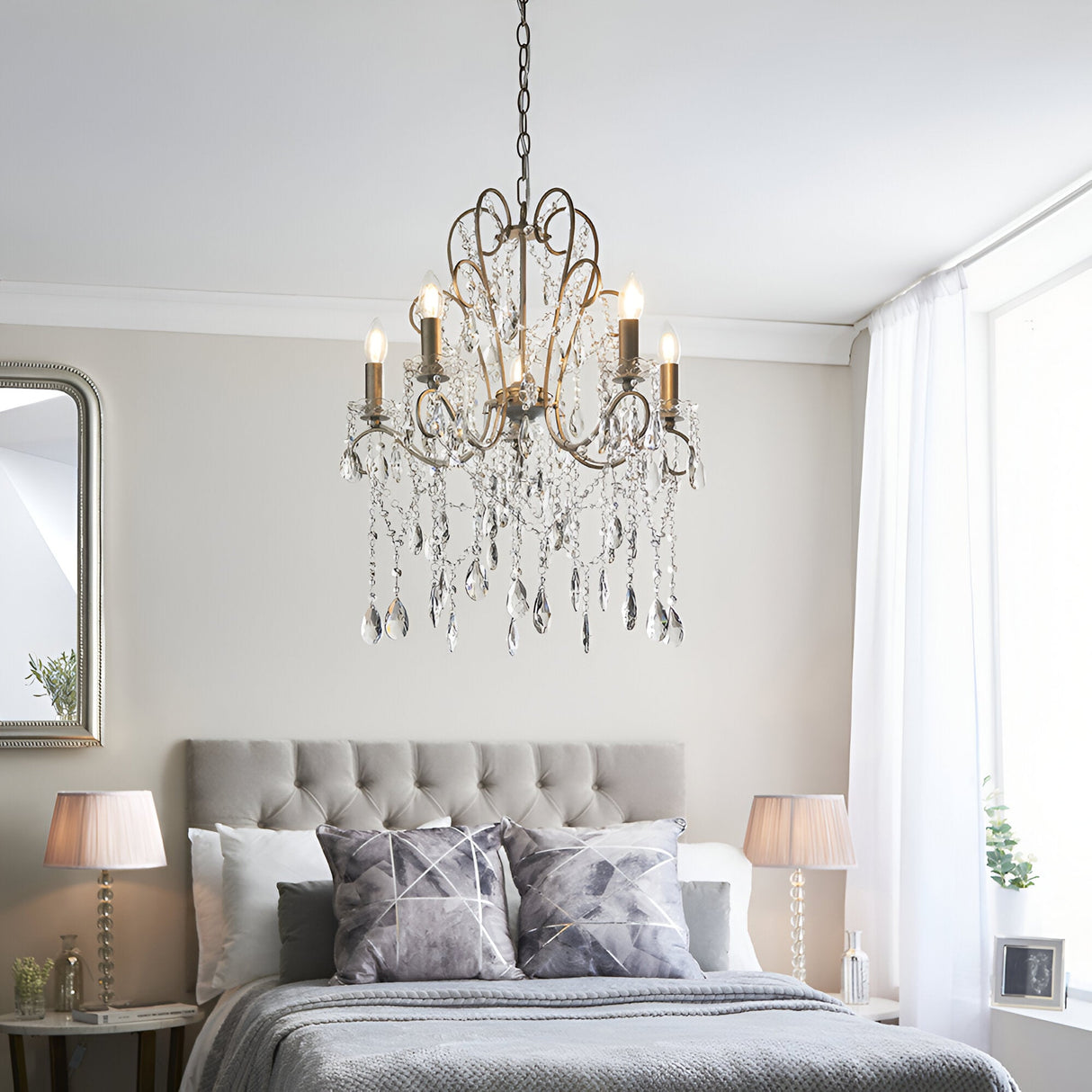 Endon Aldwood 5 light pendant in aged silver with cut crystal droplets, hanging above a grey upholstered bed between two lamps in a bedroom.