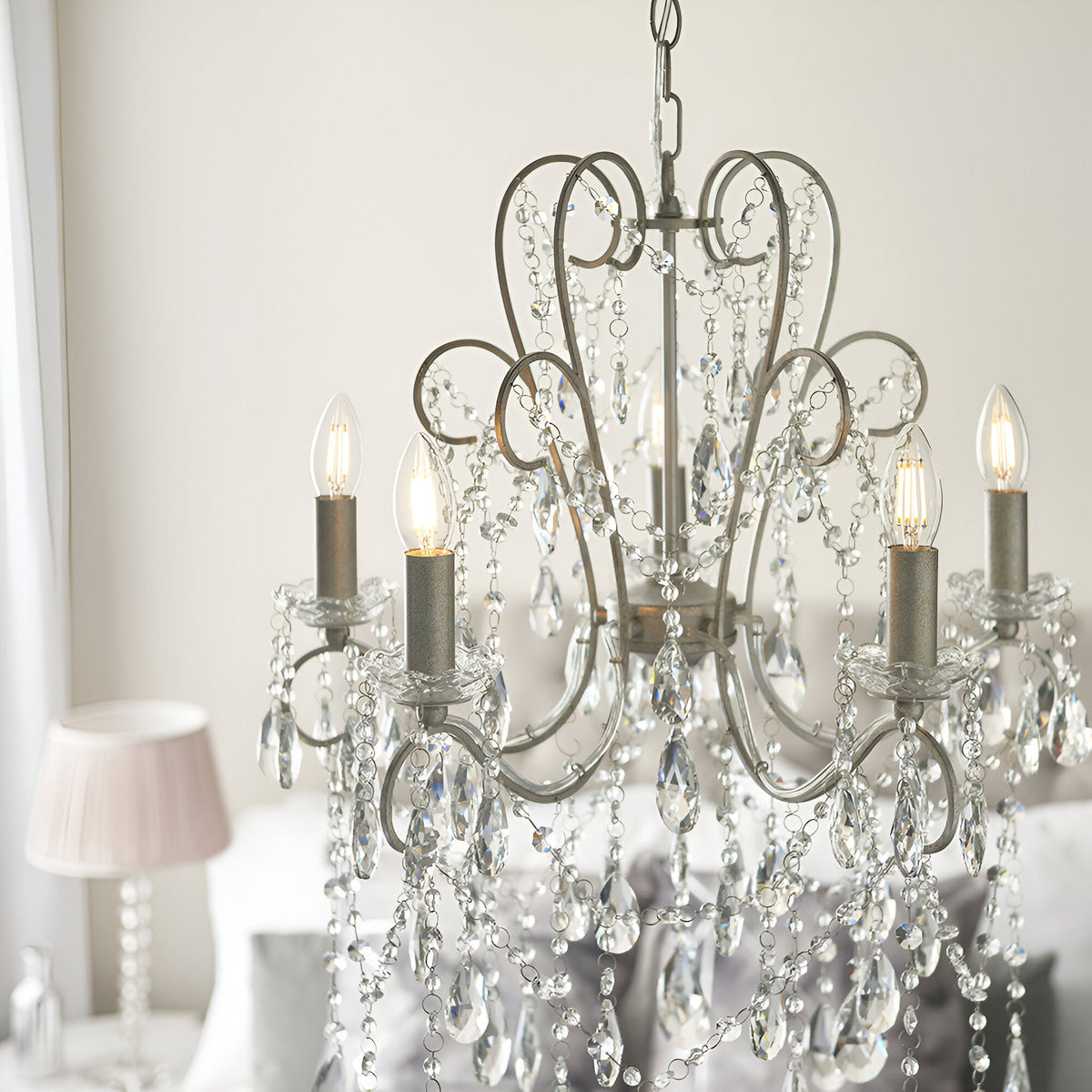 Endon Aldwood 5 light pendant in aged silver with scrolled metalwork and faceted crystal drops, hung above a bed in a soft neutral bedroom.