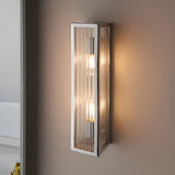 Endon Castcombe 2 light bathroom wall light in chrome with ribbed glass diffuser, mounted on a taupe wall casting a warm glow beside a mirror.