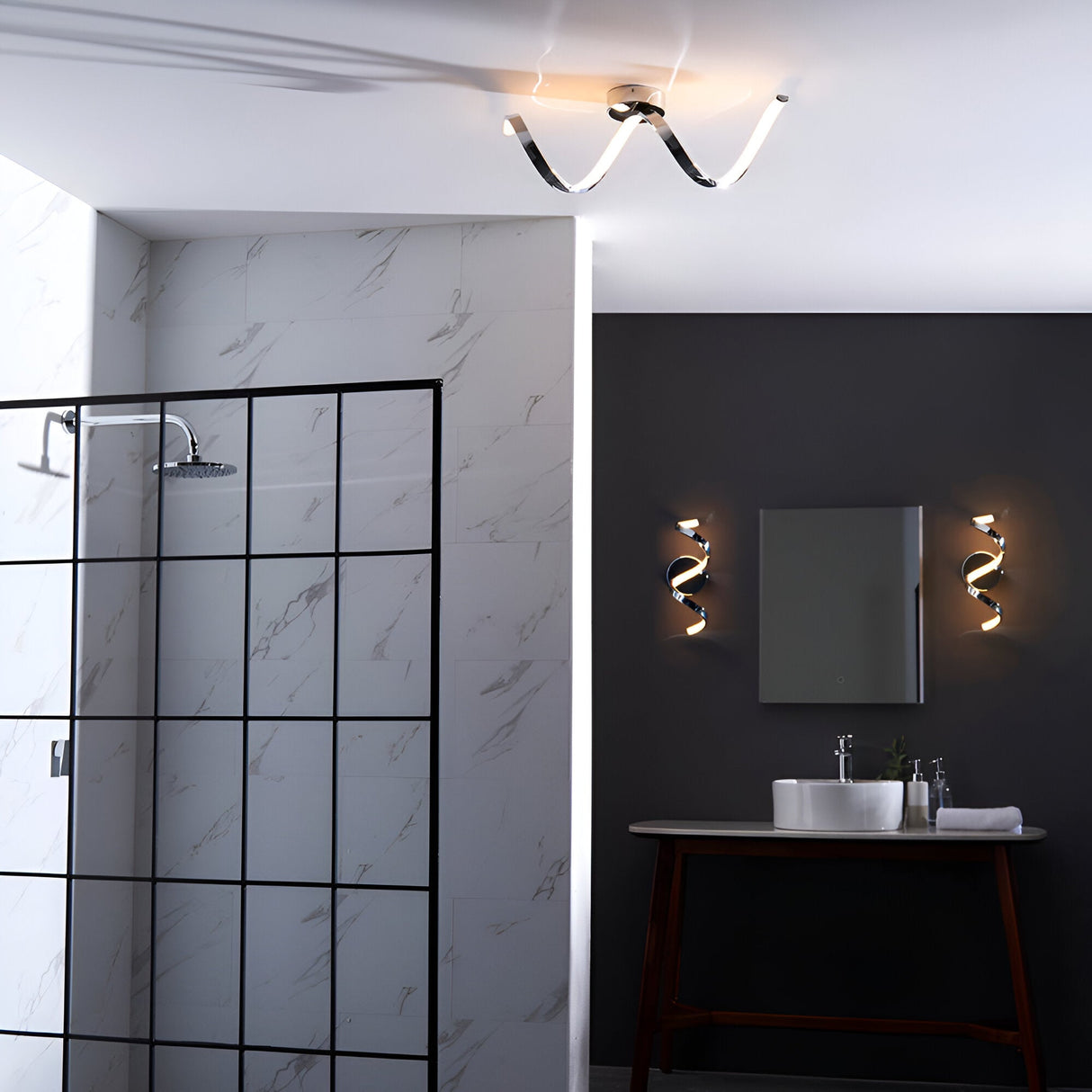 Endon Aldleigh LED wall lights in chrome twisting form flank a bathroom mirror, with a matching ceiling light above a marble walk-in shower.