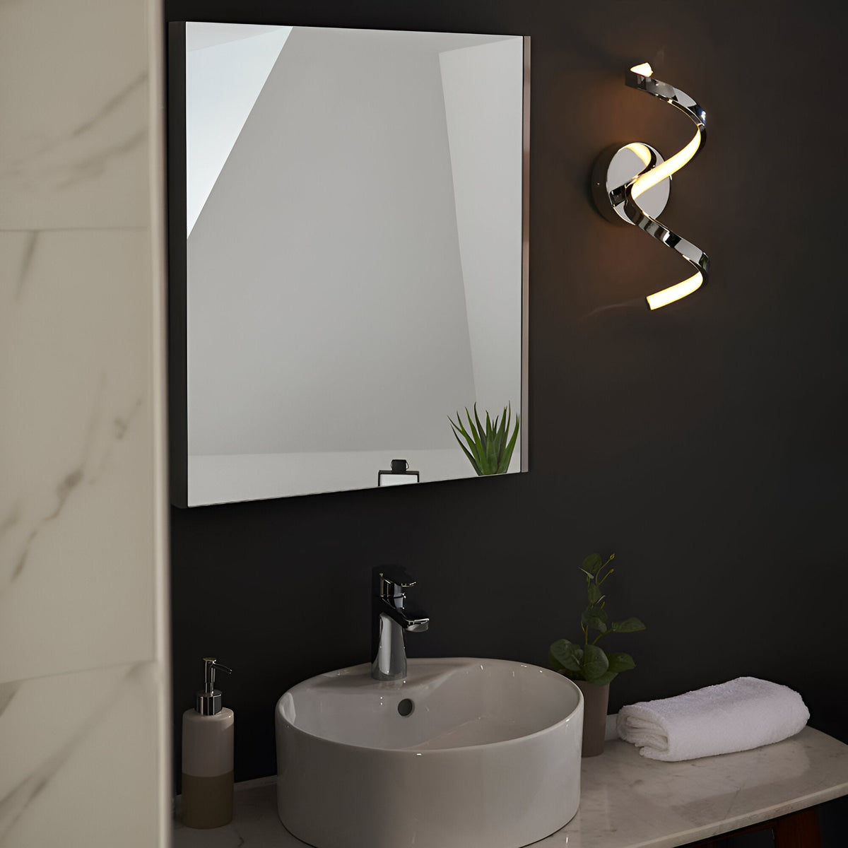 Endon Aldleigh LED wall light in chrome with a twisting spiral form, mounted beside a rectangular mirror above a round basin on a dark bathroom wall.