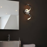 Endon Aldleigh LED wall light in chrome with a twisting spiral form and warm white glow, mounted on a dark bathroom wall beside a mirror and basin.