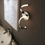 Endon Aldleigh LED wall light in chrome with a twisting spiral form and warm white glow, mounted beside a bathroom mirror above a basin.