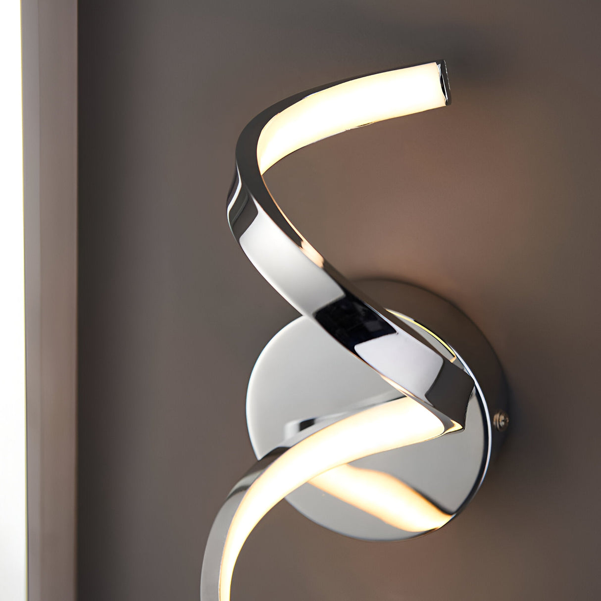 Endon Aldleigh LED wall light in chrome with a twisting spiral form and warm white glow, mounted on a circular backplate against a grey wall.