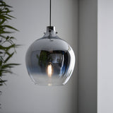 Castworth Glass Pendant in chrome, single-drop globe shade with ombre mirrored finish and visible E27 bulb, hung in a room with a green plant nearby.