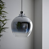 Castworth Glass Pendant in chrome, single-drop globe shade with reflective ombre finish, hung near a plant against a neutral grey wall.