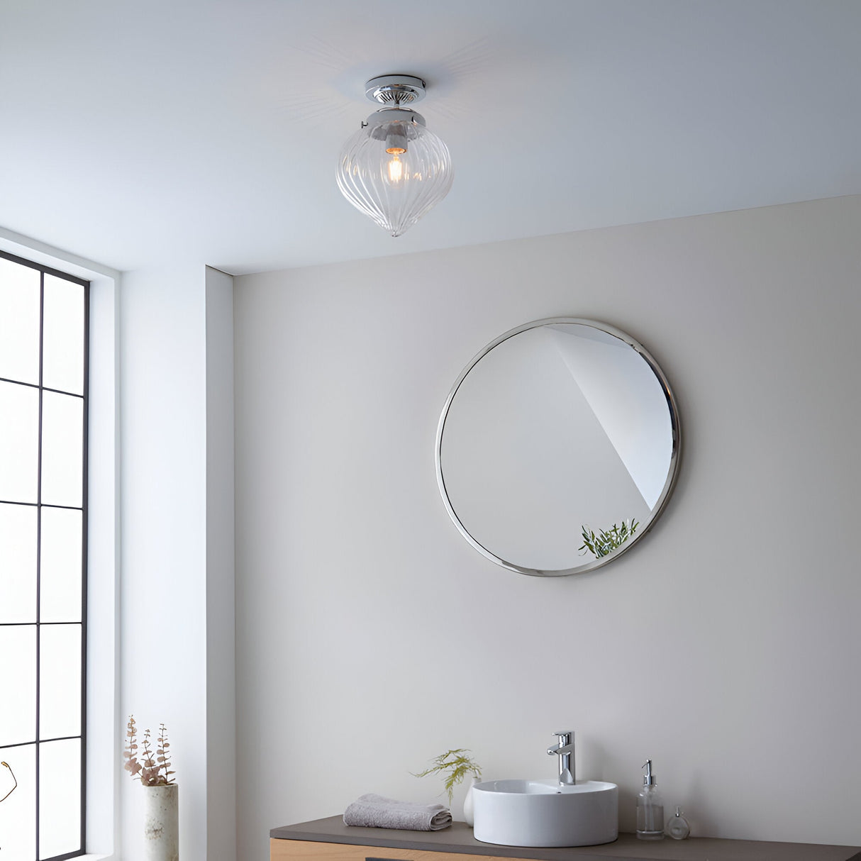 Endon Thornton flush bathroom ceiling light in chrome with a ribbed clear glass shade, mounted above a round chrome wall mirror and basin.