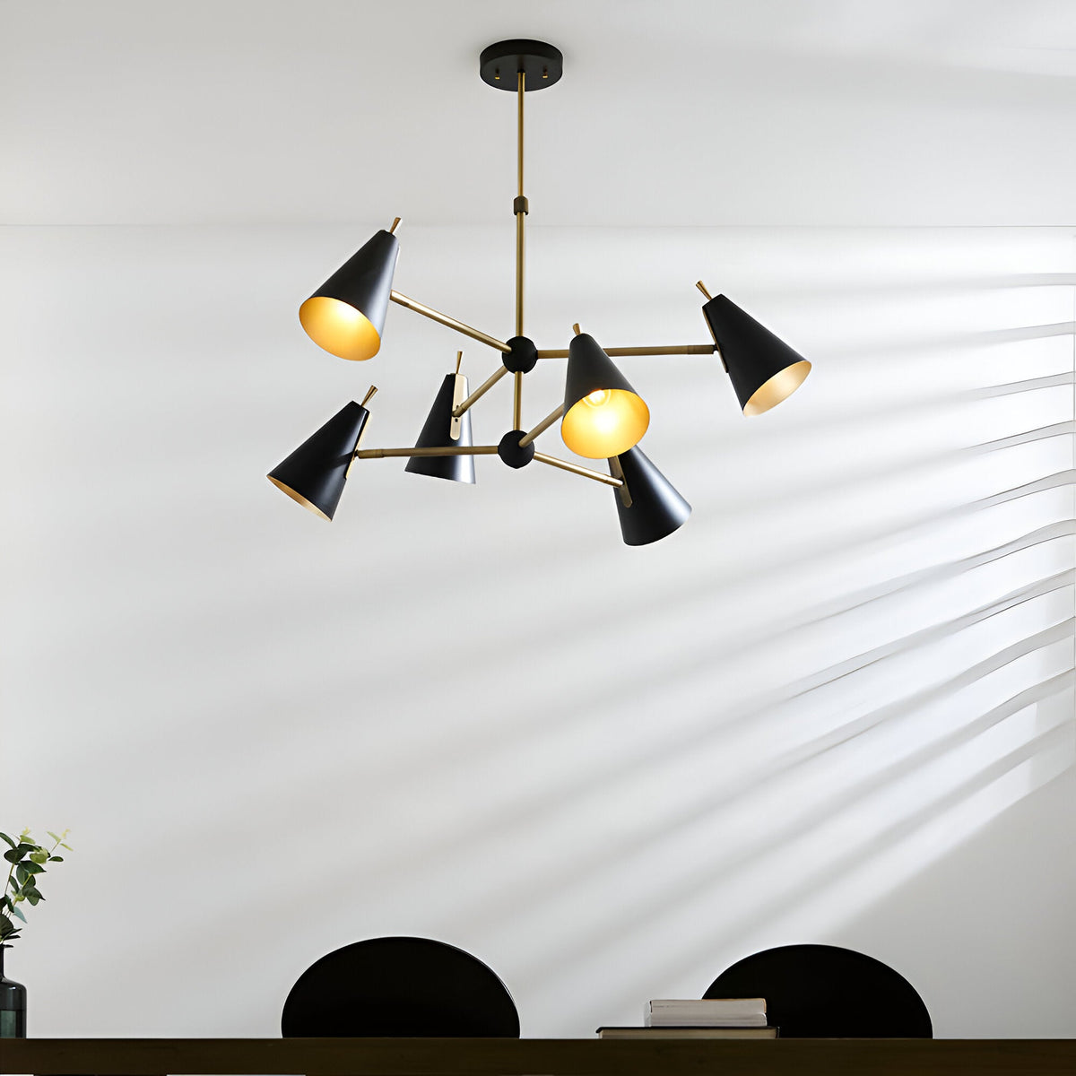 Brackwick 6-light pendant with matt black cone shades on angled brass arms, hung above a dining table with black chairs.