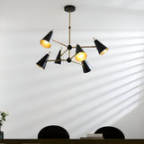 Brackwick 6-light pendant with matt black cone shades on angled brass arms, hung above a dining table with black chairs.