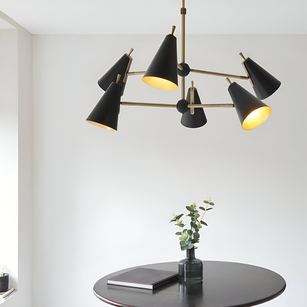 Brackwick 6 Light Pendant in matt black with brass arms and adjustable cone shades, hanging above a round dark dining table in a light-toned room.