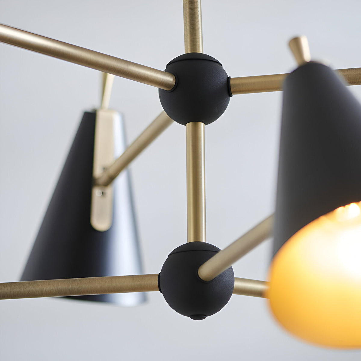 Close-up of the Brackwick 6 Light Pendant showing matt black cone shades on brushed brass arms with black ball joints, set against a plain light background.