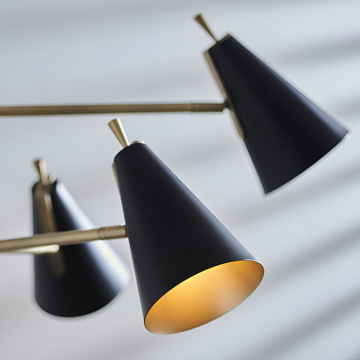 Brackwick 6 Light Pendant close-up showing matt black cone shades with brass detailing and gold interior on adjustable brass arms, plain light background.