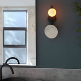 Endon Cliffshaw matt black bathroom wall light with opal glass sphere and round magnifying mirror, mounted on a dark wall beside a marble-framed window.