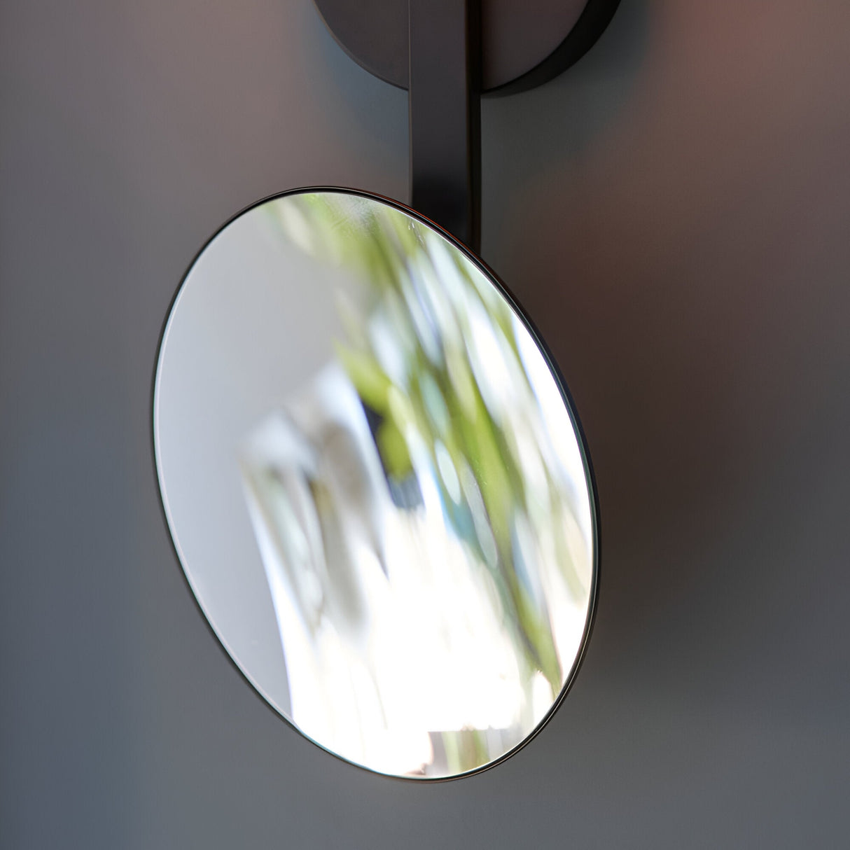 Close-up of the Endon Cliffshaw bathroom wall light's adjustable round magnifying mirror on a matt black arm, mounted against a soft grey wall.