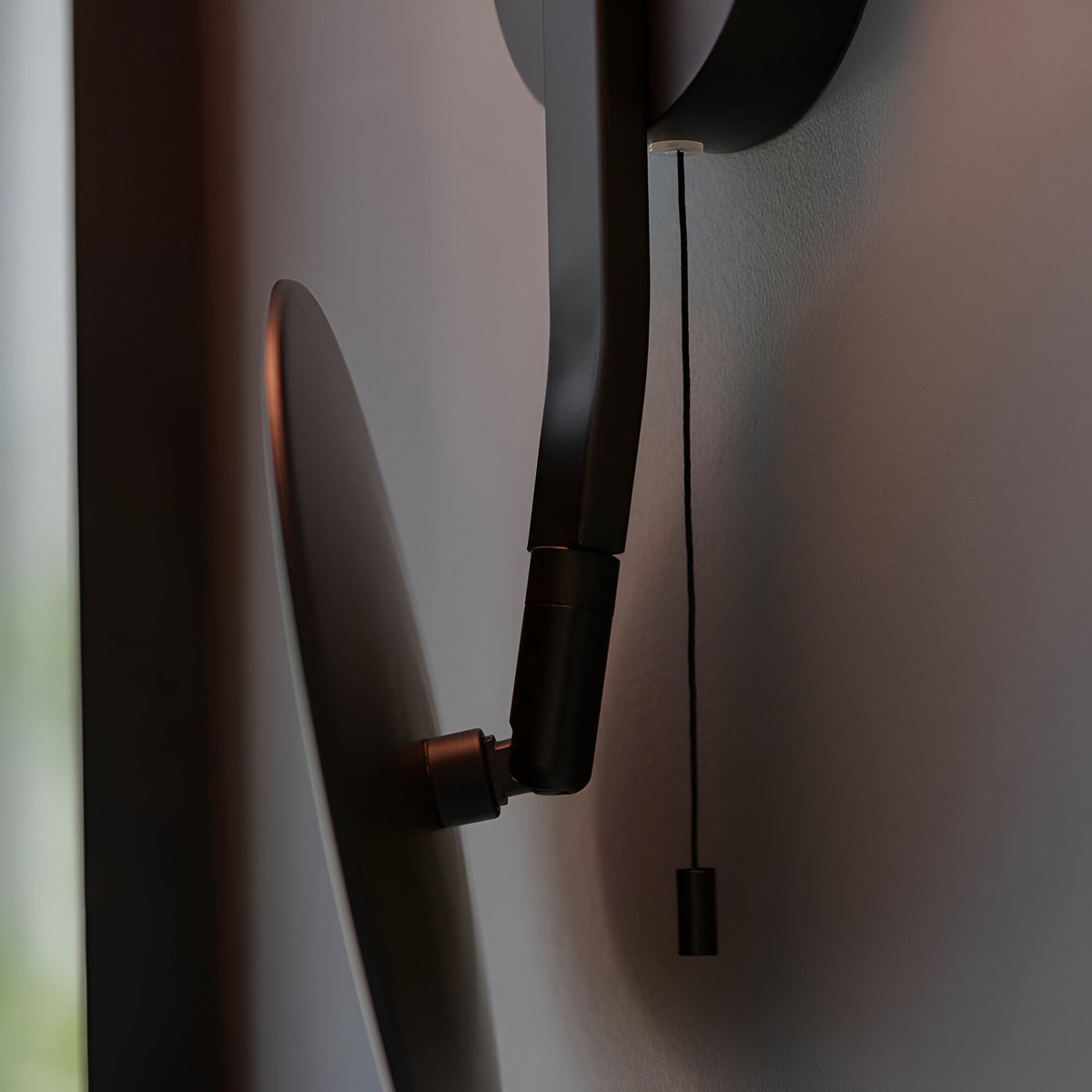 Close-up of the Endon Cliffshaw matt black bathroom wall light showing the adjustable mirror arm joints and pull cord switch against a pale wall.