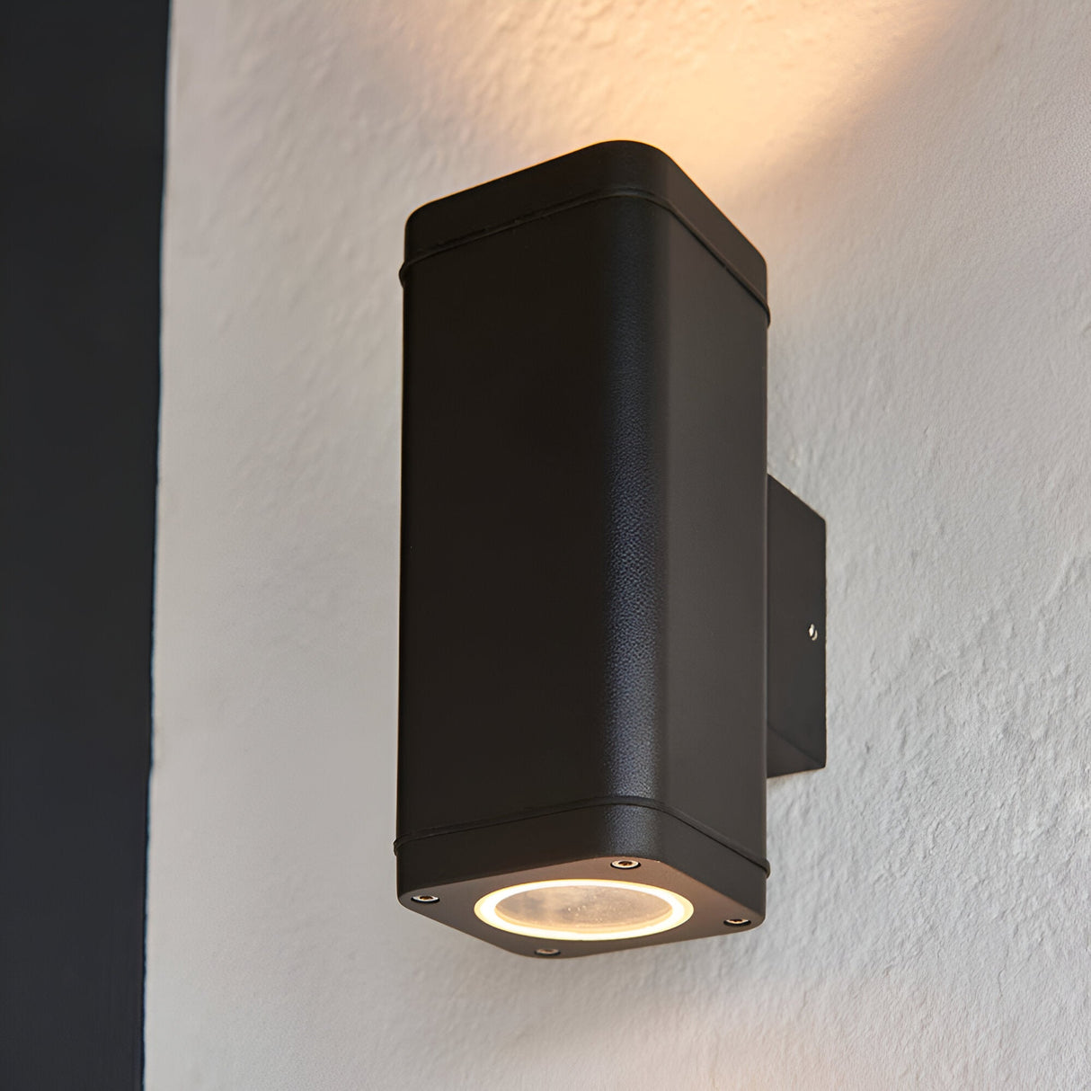 Carlford 2 Light Outdoor Wall Light in black, rectangular textured aluminium body mounted on a light wall, casting light up and down.