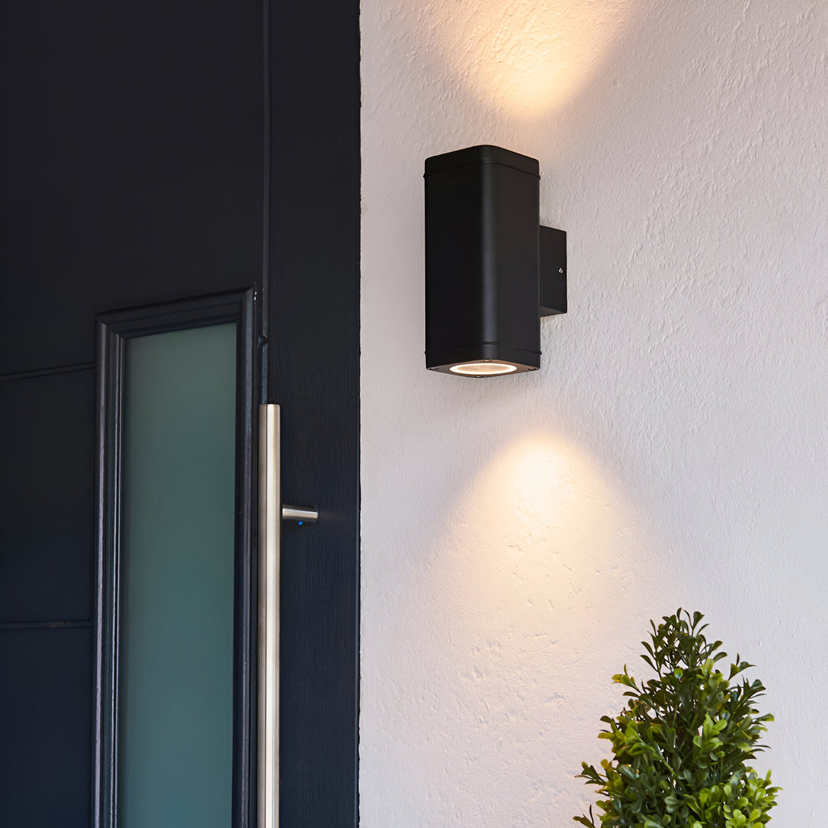 Carlford 2 Light Outdoor Wall Light in black aluminium, mounted beside a front door, casting up and down light on a textured white wall.