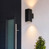 Carlford 2 Light Outdoor Wall Light in black aluminium, mounted beside a front door, casting up and down light on a textured white wall.