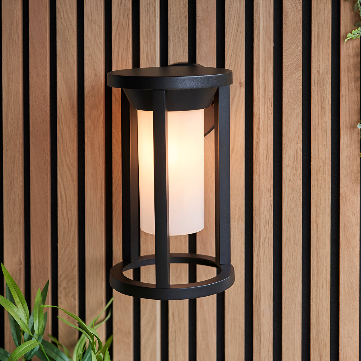 Endon Ashdale outdoor wall light with black aluminium cage frame and white polycarbonate cylinder shade, mounted on a slatted wood wall.