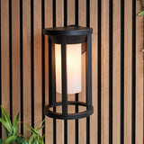 Endon Ashdale outdoor wall light with black aluminium cage frame and white polycarbonate cylinder shade, mounted on a slatted wood wall.