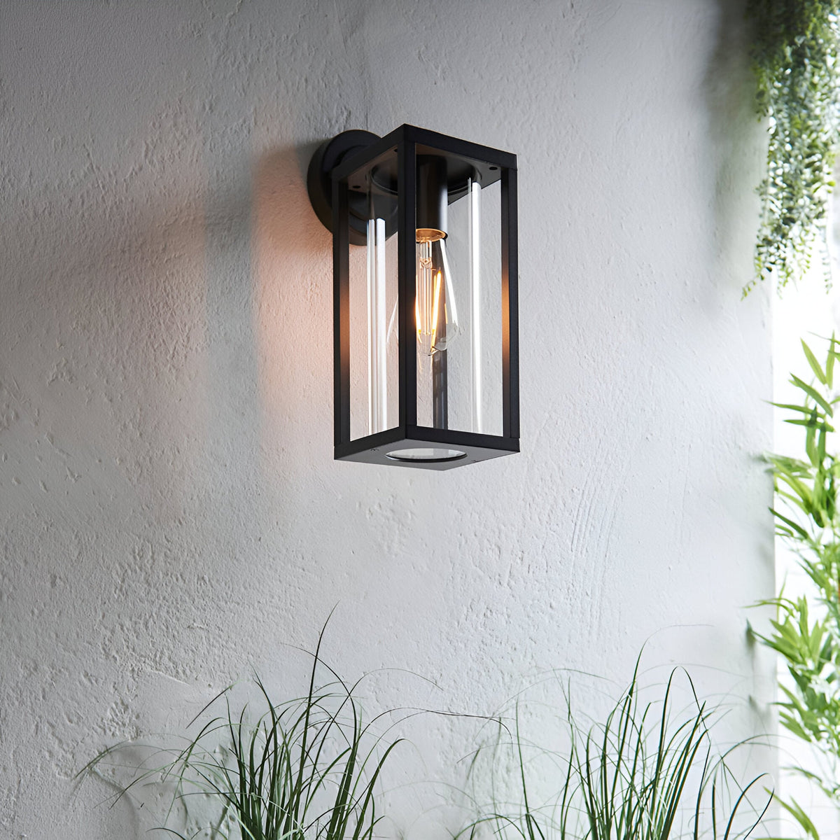 Endon Bramwood outdoor wall light in textured black with slim rectangular lantern frame, clear glass panels and E27 filament bulb, mounted on a pale wall.