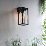 Endon Bramwood outdoor wall light in textured black with slim rectangular lantern frame, clear glass panels and E27 filament bulb, mounted on a pale wall.