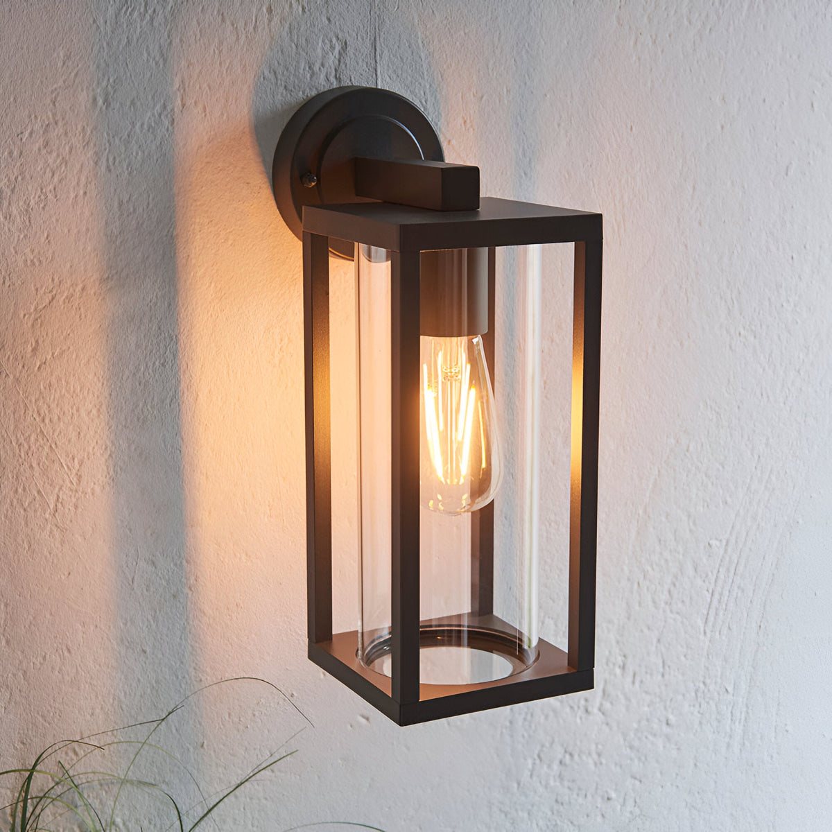 Endon Bramwood outdoor wall light in textured black with clear glass panels and a warm filament E27 bulb, mounted on a pale rendered wall.