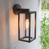 Endon Bramwood outdoor wall light in textured black aluminium with clear glass panels and a warm filament E27 bulb, mounted on a white exterior wall.
