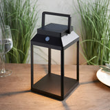 Caldshaw LED Solar Table Lamp in black, lantern-style aluminium frame with white diffuser panel and carry handle, shown lit on a wooden table.