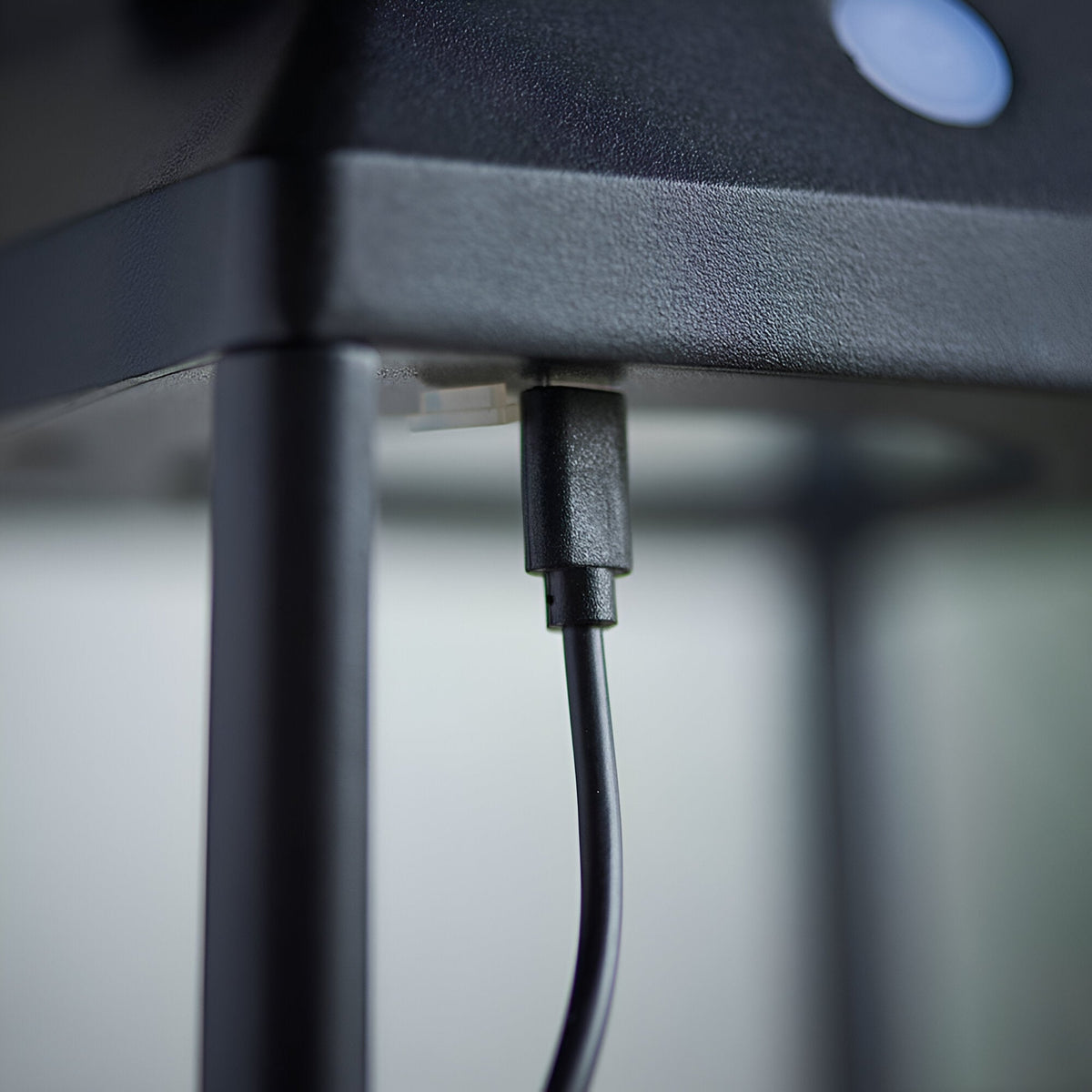 Close-up of the Caldshaw LED Solar Table Lamp in black showing the USB charging port and cable beneath the textured metal base.