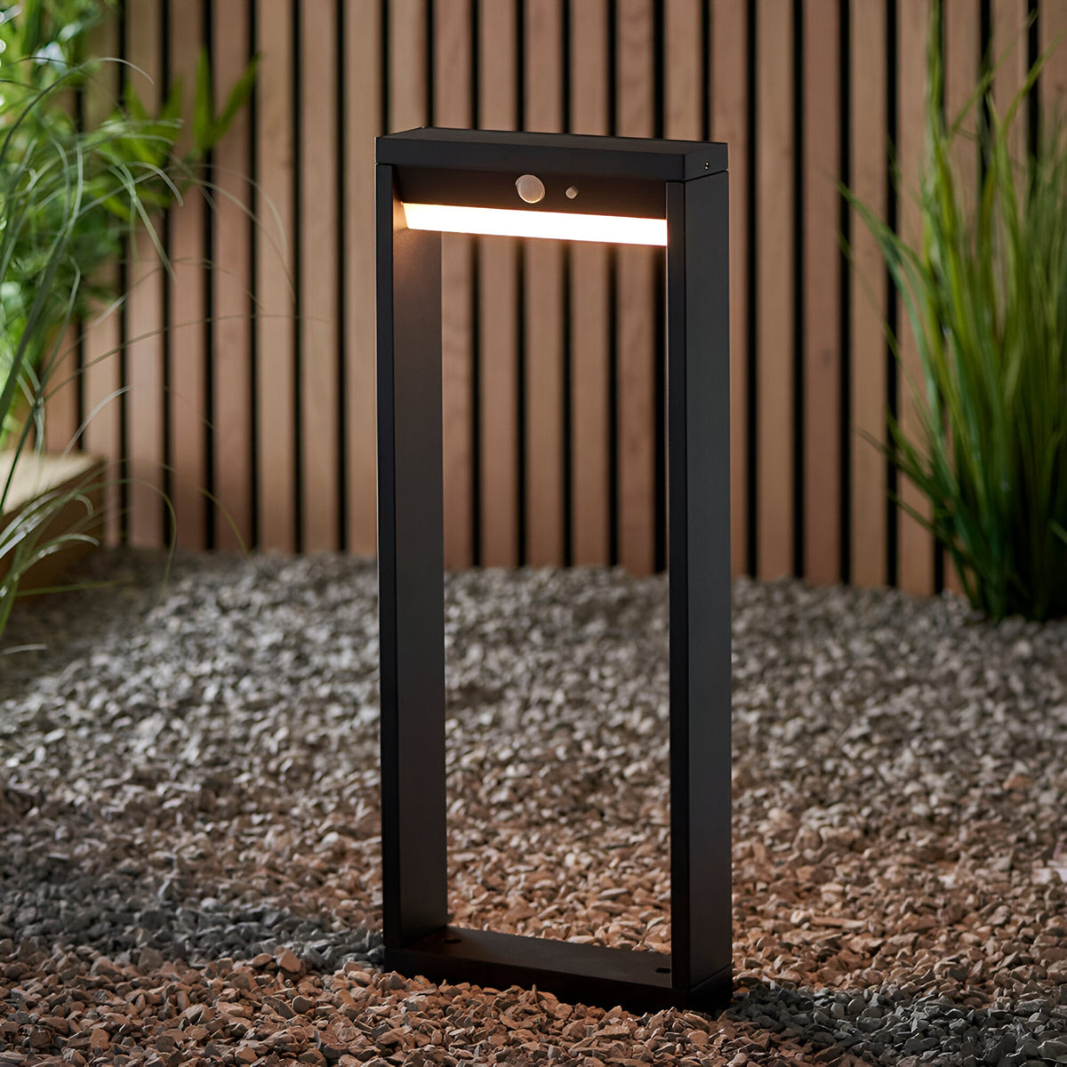 Endon Blythe LED solar post light in matte black aluminium with warm white diffuser and PIR sensor, on gravel beside a slatted wood fence and grasses.