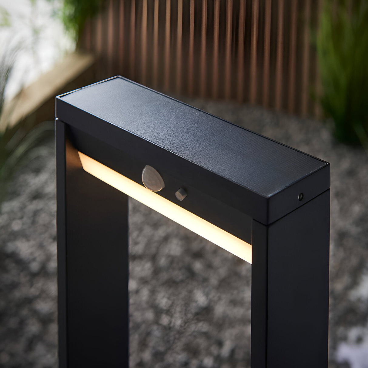 Close-up of Endon Blythe LED solar post light in textured black aluminium, showing warm white diffuser, PIR sensor and solar panel top, set on gravel.