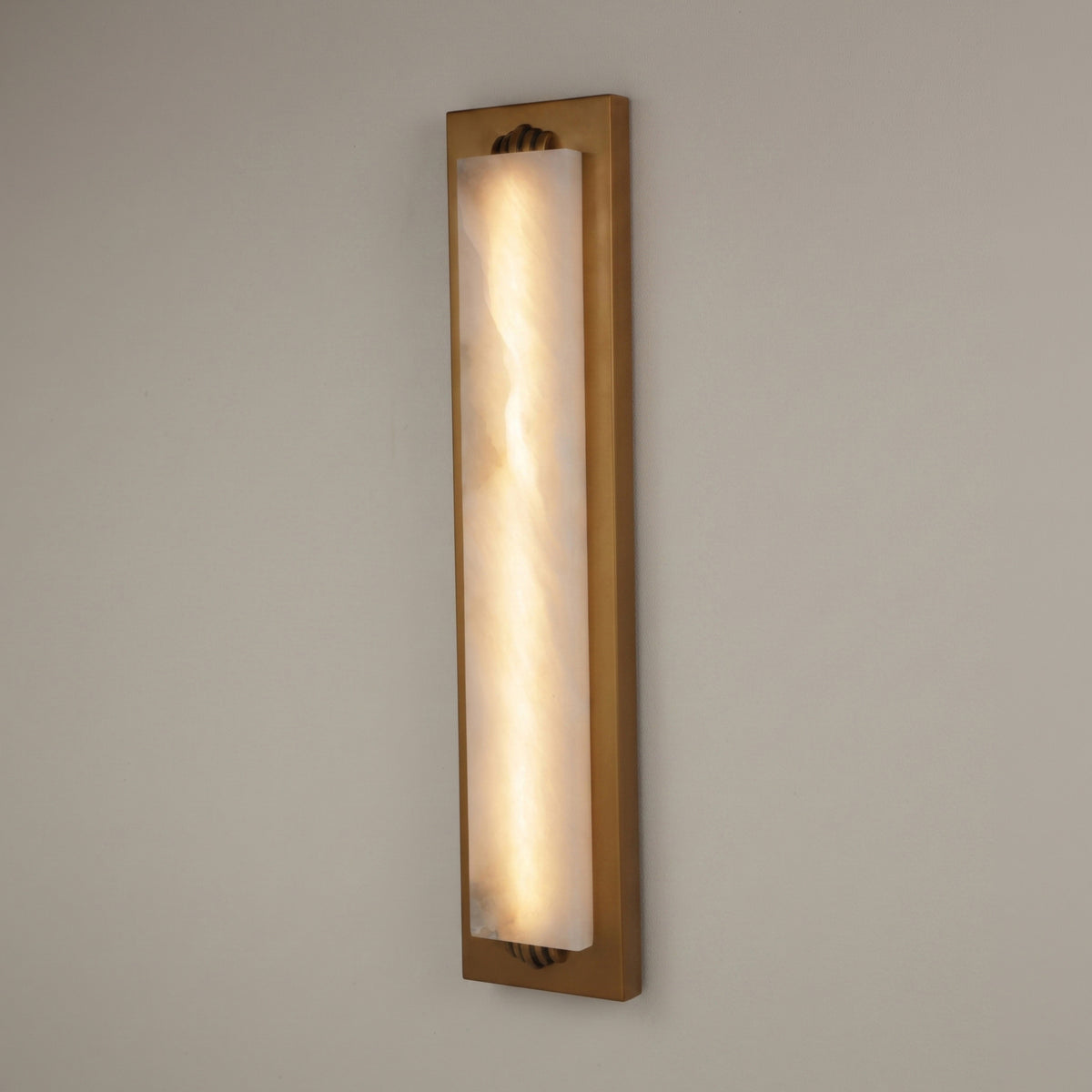 Valora vertical wall light with tall alabaster panel glowing warm white within a brushed brass rectangular frame, shown against a plain light background.