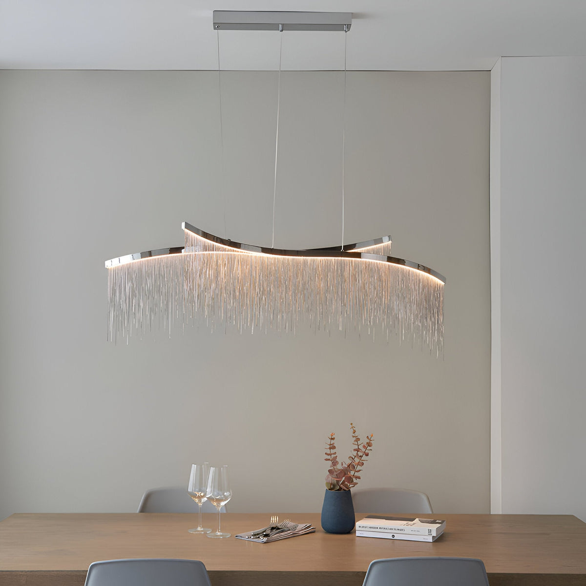 Endon Caststead linear pendant in polished chrome with cascading silver chain fringe and integrated LED, suspended above a wooden dining table.