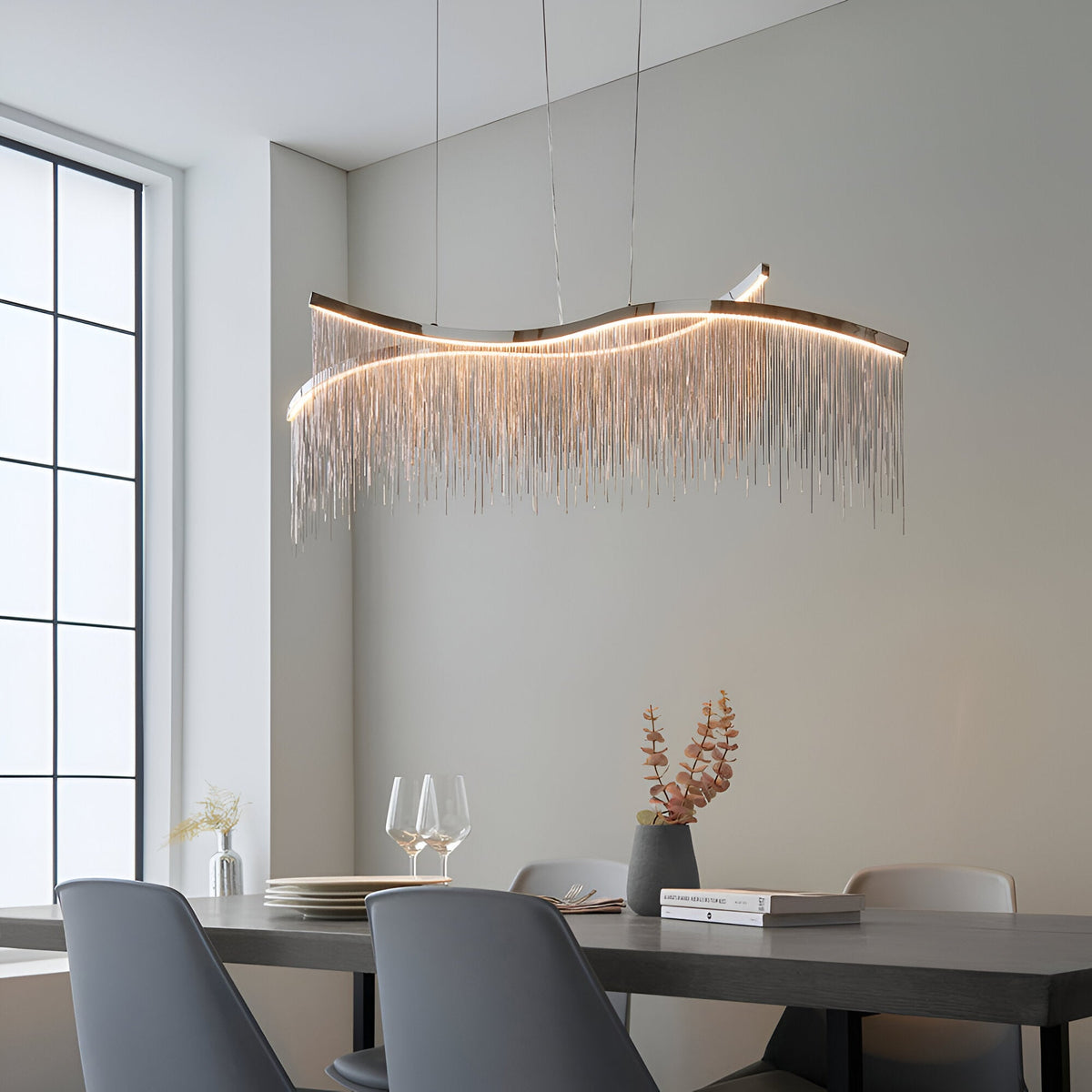 Endon Caststead linear pendant in polished chrome with a wavy bar and cascading silver chain fringe, suspended above a dining table with grey chairs.