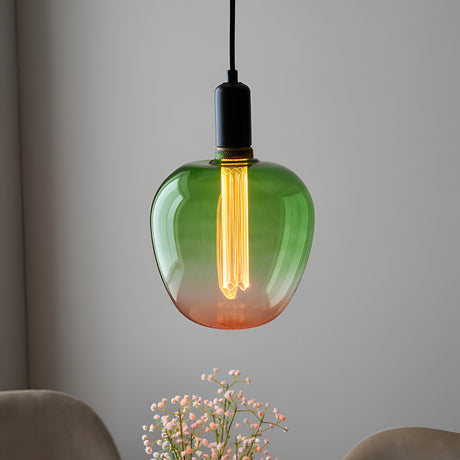 Endon 2.8W E27 LED filament bulb with green-to-pink ombre glass, glowing warm white in a black pendant fitting above pale flowers.