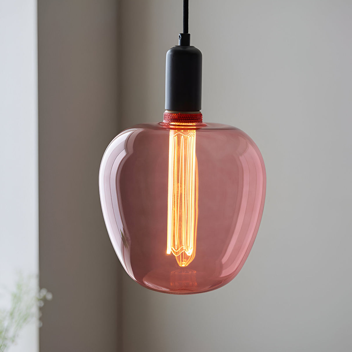 Pendant light with pink-tinted glass shade and black fitting, showing a lit 2.8W E27 LED filament bulb, warm white glow, in a neutral room.