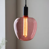 Pendant light with pink-tinted glass shade and black fitting, showing a lit 2.8W E27 LED filament bulb, warm white glow, in a neutral room.