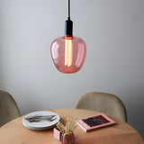 Pink-tinted E27 LED filament bulb glowing warm white in a globe pendant light above a wooden dining table with plates and a vase.