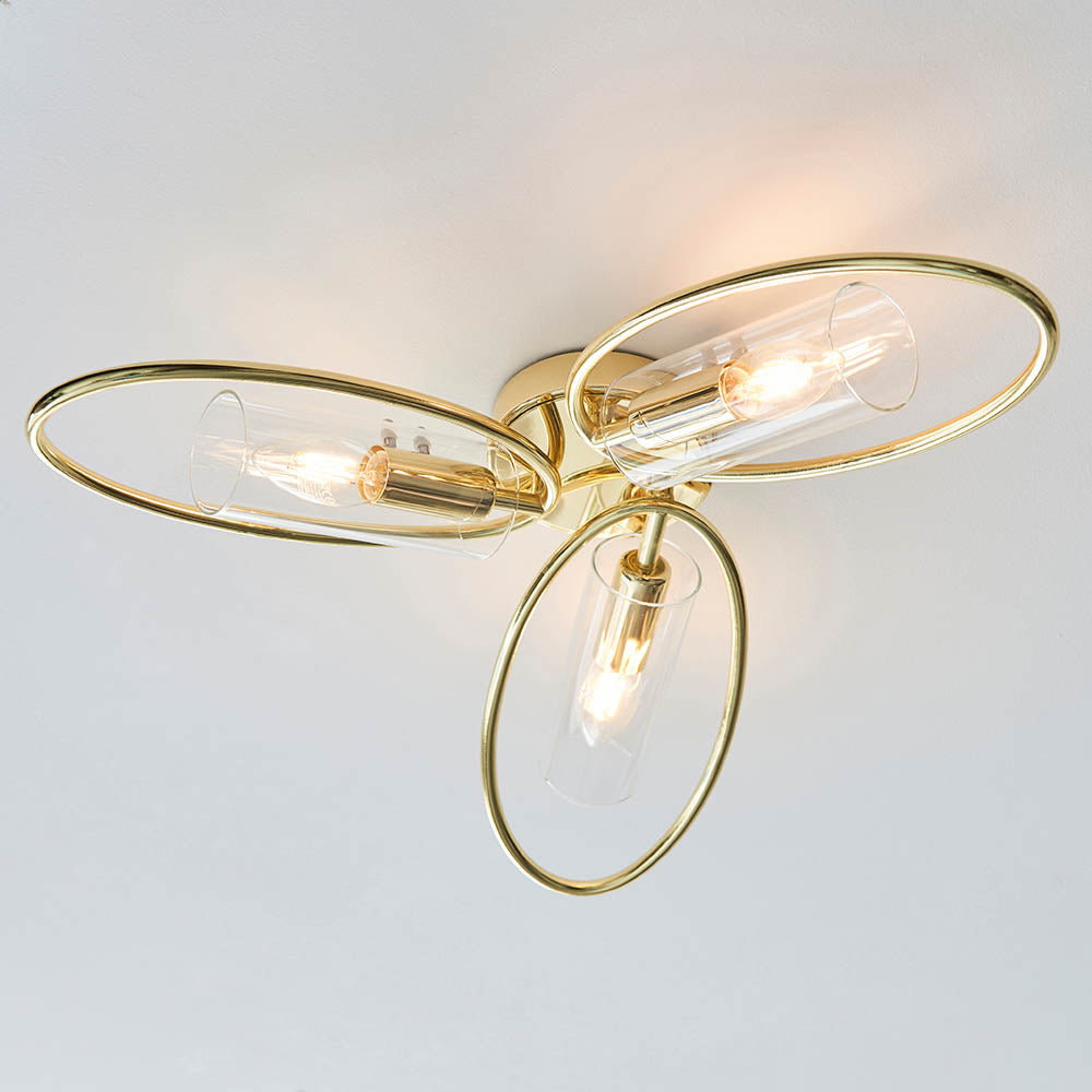 Endon Hartley 3 light semi-flush ceiling light with brass oval rings and clear glass cylinder shades, illuminated against a white ceiling.