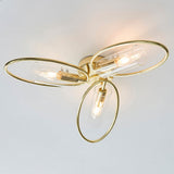 Endon Hartley 3 light semi-flush ceiling light with brass oval rings and clear glass cylinder shades, illuminated against a white ceiling.