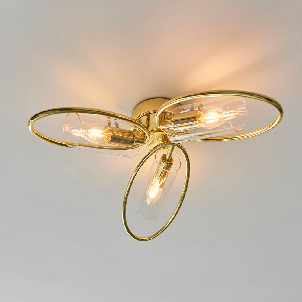 Endon Hartley 3 light semi-flush ceiling light in brass, with three oval rings holding clear glass shades and lit E14 lamps against a white ceiling.