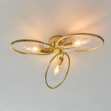 Endon Hartley 3 light semi-flush ceiling light in brass, with three oval rings holding clear glass shades and lit E14 lamps against a white ceiling.