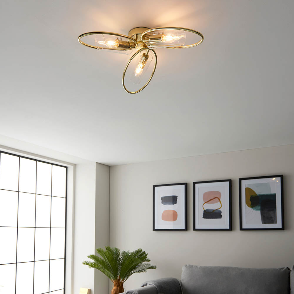 Endon Hartley 3 light semi-flush ceiling light in brass with three interlinked rings and glass shades, shown lit in a living room with framed art.