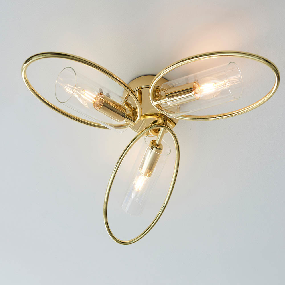 Endon Hartley 3 light semi-flush ceiling light in brass with three oval rings and clear glass shades, viewed from below against a pale ceiling.
