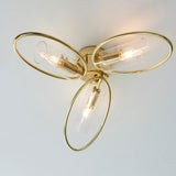 Endon Hartley 3 light semi-flush ceiling light in brass with three oval rings and clear glass shades, viewed from below against a pale ceiling.