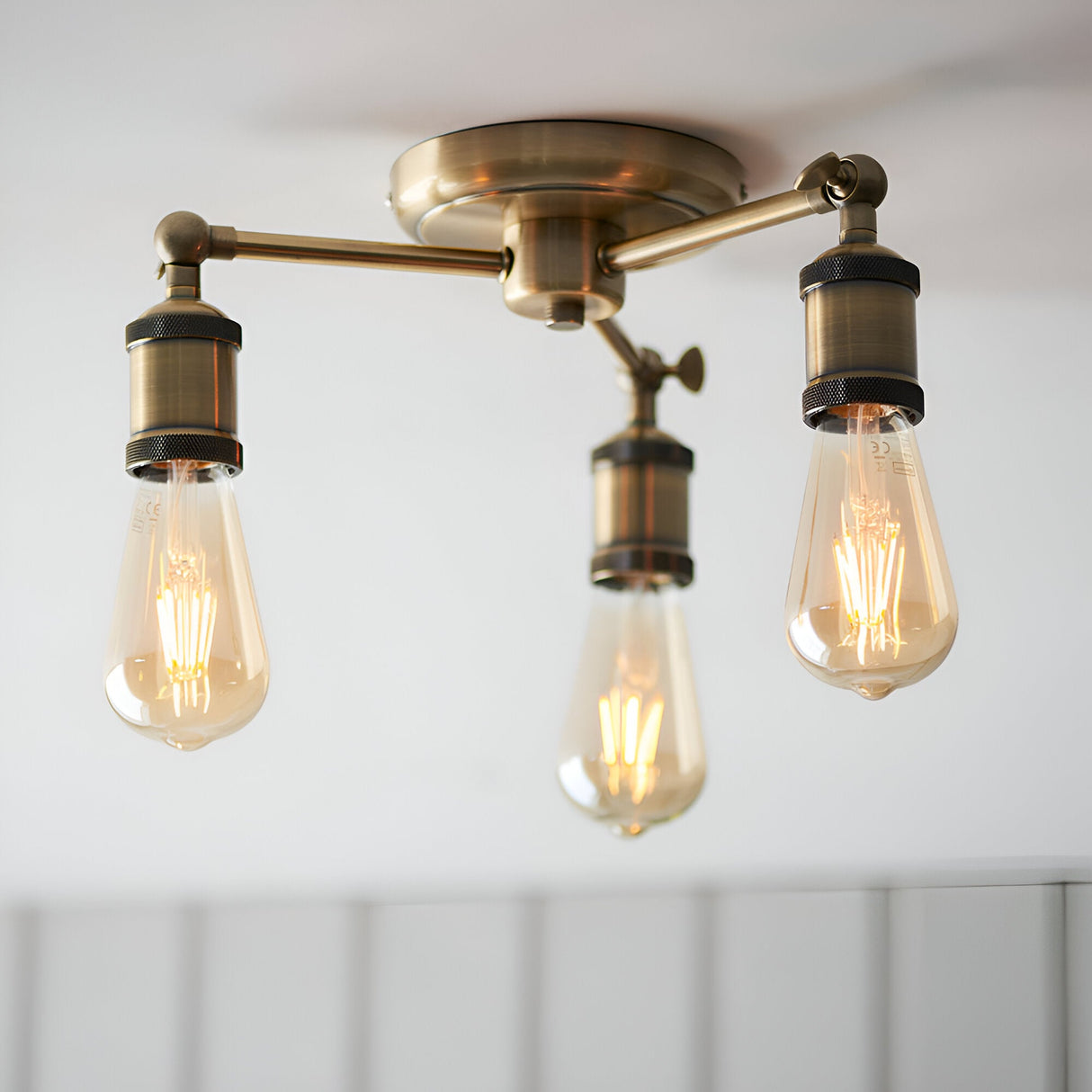 Endon Brackley 3 light semi-flush ceiling light in brass, with three outward arms holding exposed teardrop Edison bulbs against a white ceiling.