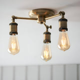 Endon Brackley 3 light semi-flush ceiling light in brass, with three outward arms holding exposed teardrop Edison bulbs against a white ceiling.
