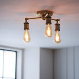 Endon Brackley 3 Light semi-flush ceiling light in brass with three outward arms and exposed E27 filament bulbs, mounted to a white ceiling.